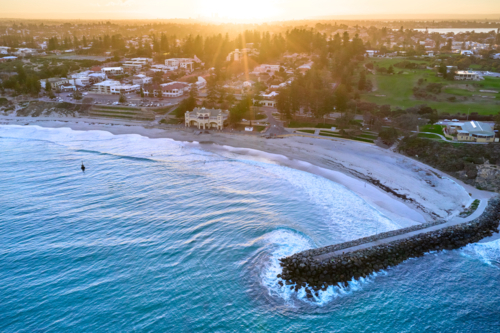 The sun rising on the horizon with an aerial view of Perth's famous Cottesloe beach - Australian Stock Image