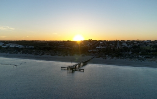 The sun rising over the horizon, with a view across the water and jetty at Coogee Beach, Perth - Australian Stock Image