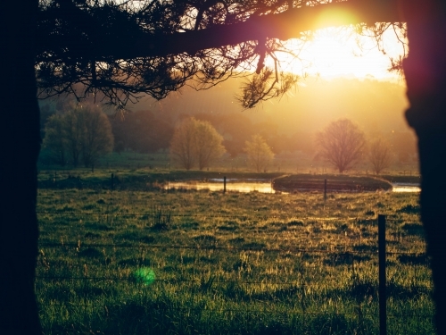The sun setting over a dam on a farm - Australian Stock Image
