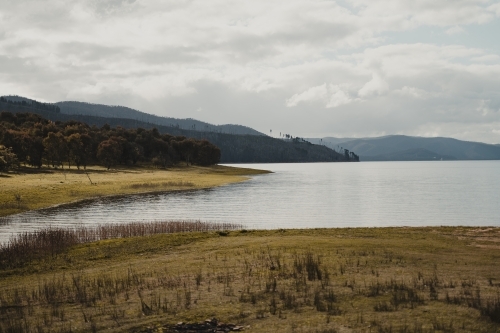 The water's edge with mountains in the background at Blowering Reservoir - Australian Stock Image