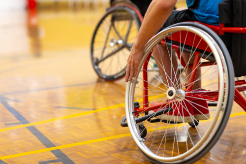 the wheel of a wheelchair is the focus and a hand pushes the wheel on a basketball court - Australian Stock Image