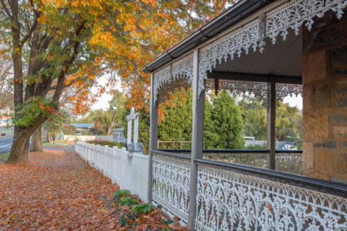 The wrought iron verandah of an old country home underneath orange leaves - Australian Stock Image
