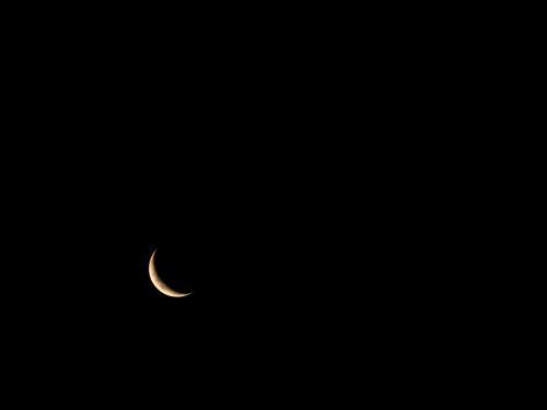 Thin crescent moon in a very dark sky in bottom left corner - Australian Stock Image