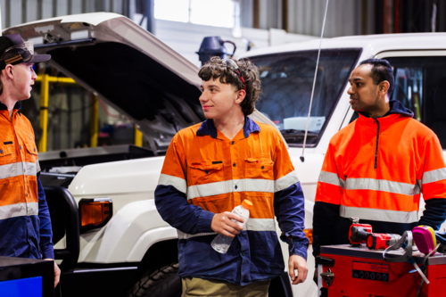 Three Australian men in industrial mechanics shed workplace chatting in conversation together - Australian Stock Image