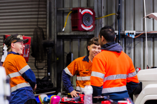 Three Australian men in industrial mechanics shed workplace chatting in conversation together - Australian Stock Image