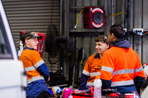 Three Australian men in industrial mechanics shed workplace chatting in conversation together - Australian Stock Image