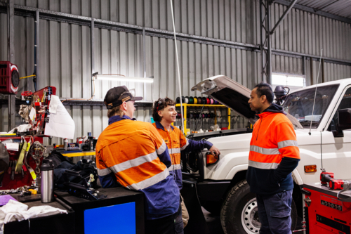 Three Australian men in industrial mechanics shed workplace chatting in conversation together - Australian Stock Image