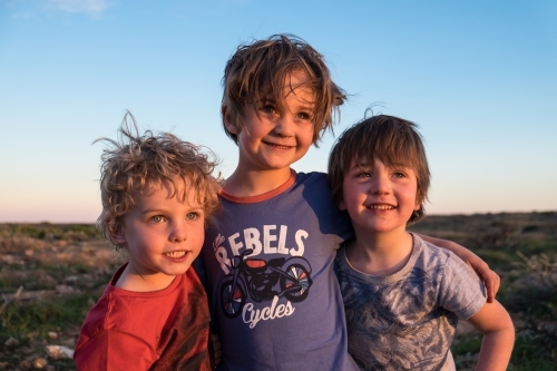 Three boys embracing at sunset