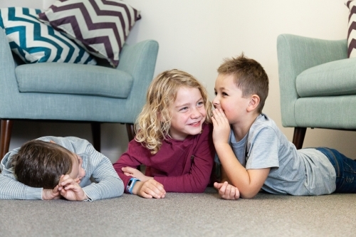 Three boys whispering and laughing with one another on floor - Australian Stock Image