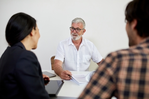 Three business people sitting at a desk, talking in a studio - Australian Stock Image