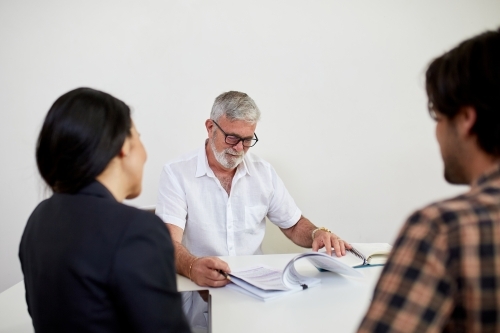 Three business people sitting at a desk, talking in a studio - Australian Stock Image