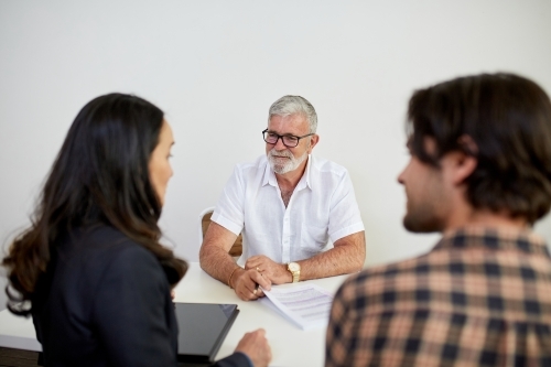Three business people sitting at a desk, talking in a studio - Australian Stock Image