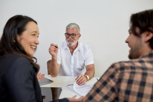 Three business people sitting at a desk, talking in a studio - Australian Stock Image