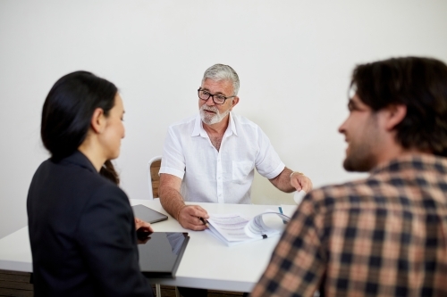 Three business people sitting at a desk, talking in a studio - Australian Stock Image
