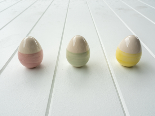 Three ceramic easter eggs with pastel stripes on white timber table top - Australian Stock Image