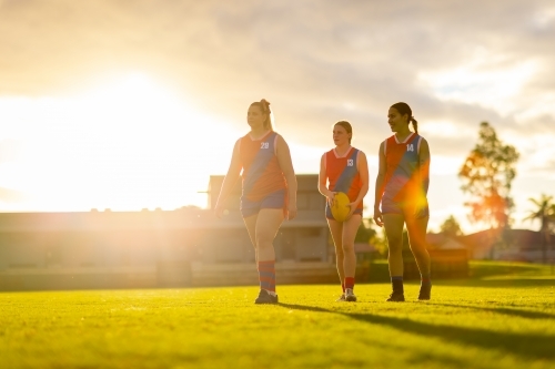 three female football players walking off oval with golden backlight