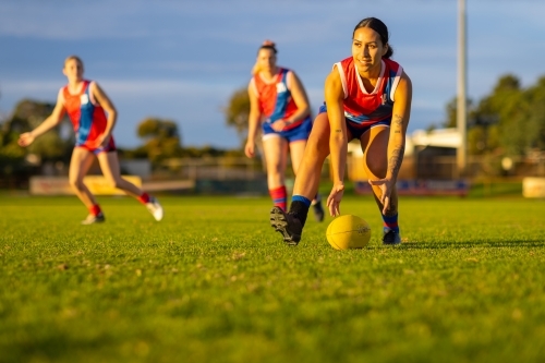 three female footballers in red and blue uniforms playing aussie rules footbal