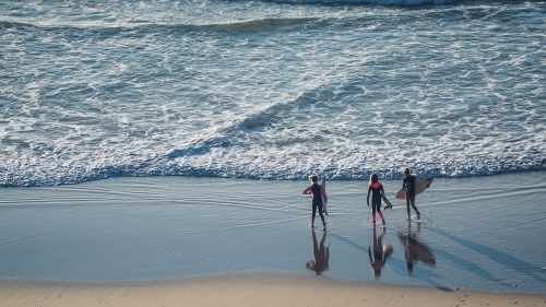 Three female surfers entering the ocean
