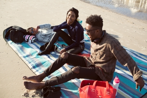 Three friends on a picnic blanket relaxing at the beach - Australian Stock Image