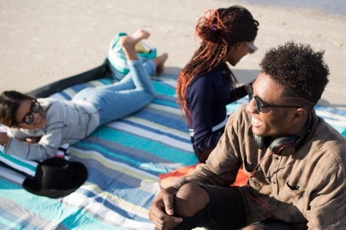 Three friends sitting on a picnic blanket at the beach - Australian Stock Image