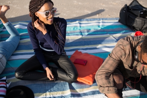 Three friends sitting on a picnic blanket relaxing at the beach - Australian Stock Image