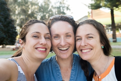 Three friends standing close together smiling at the park. - Australian Stock Image