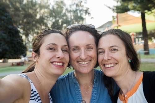 Three friends standing close together smiling at the park. - Australian Stock Image