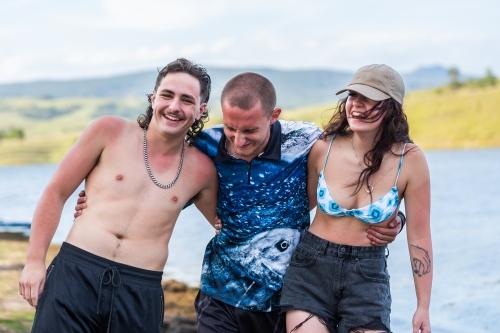 Three happy Aussie teenagers laughing together by lake in summer - Australian Stock Image