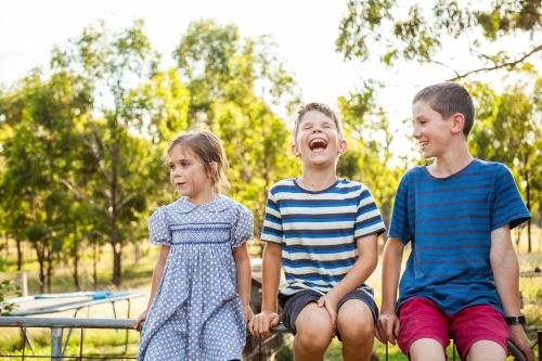 Three happy children laughing together outside - Australian Stock Image