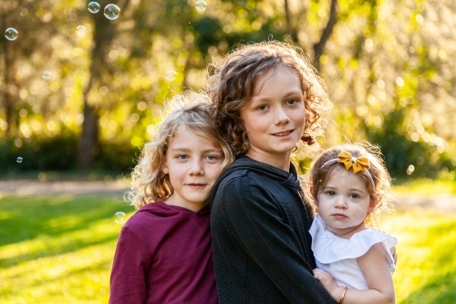 Three happy siblings with curly hair smiling at camera in park