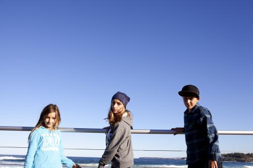 Three kids against a railing in the sunshine - Australian Stock Image