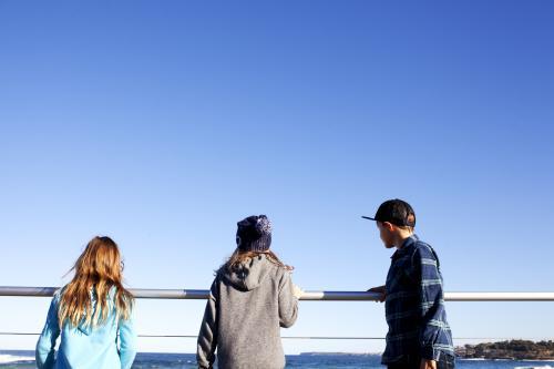 Three kids looking out over railing at ocean - Australian Stock Image