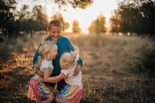 Three kids playing and hugging outside - Australian Stock Image