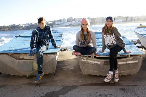 Three kids posing on boats by the ocean - Australian Stock Image