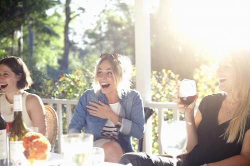 Three laughing women sitting on verandah having drinks