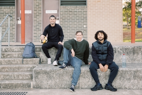 Three mates sitting on  soccer club steps, with one man holding a soccer ball
