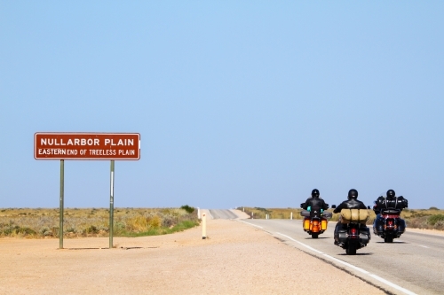 Three motorcycles pass the sign for the eastern end of the Nullarbor Plain