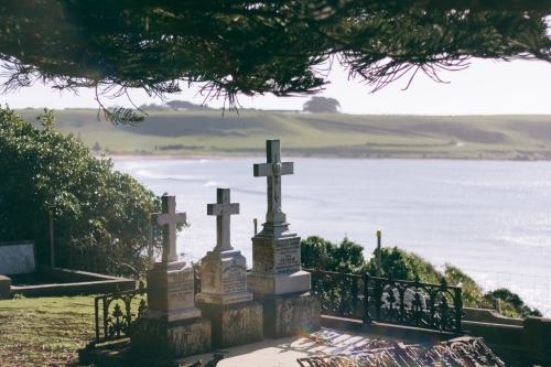 Three old headstones in a graveyard with the ocean in the background