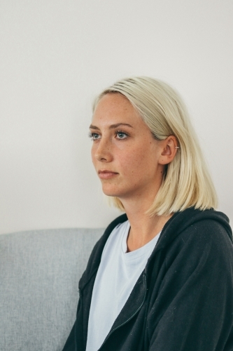Three quarter profile of young blonde woman in hoodie and t-shirt looking away - Australian Stock Image