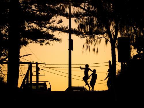 Three silhouetted kids playing in the glow of dusk with power lines
