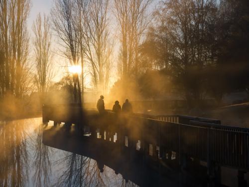 Three silhouetted people walking across a misty bridge - Australian Stock Image