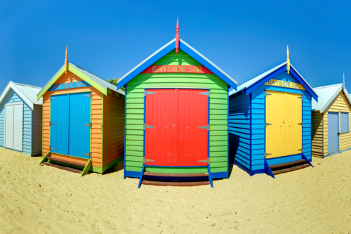 Three vibrant beach huts standing side by side on sandy shore - Australian Stock Image