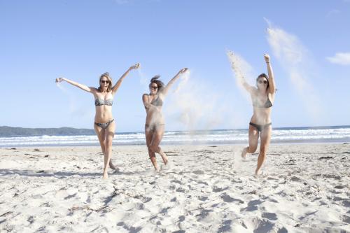 Three women running on beach throwing sand