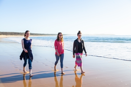 Three young adults walking along the beach seaside scene - Australian Stock Image