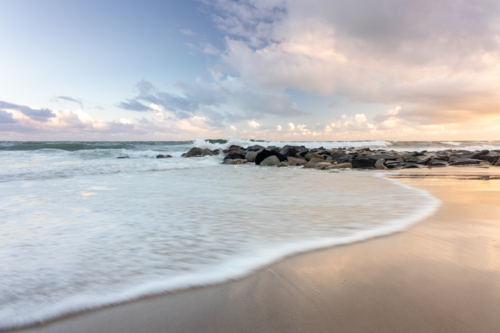 Tide coming in on beach at sunset with rock wall  in background - Australian Stock Image