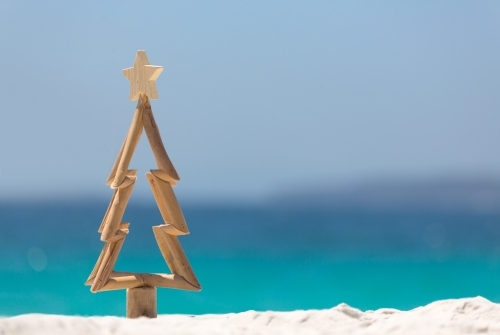 Timber Christmas tree with star sits in pristine white sand with idyllic beach background
