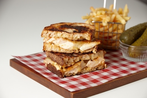 Toasted chicken sandwich with chips and pickled cucumber served on a wooden board - Australian Stock Image