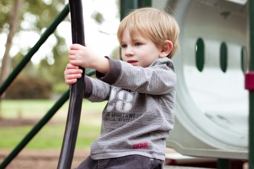 Toddler boy holding on to playground equipment
