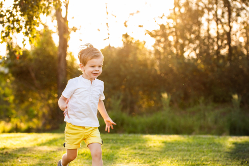 Toddler boy running through parkland in golden light with bokeh backdrop copy space - Australian Stock Image
