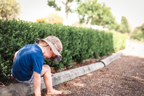 Toddler boy sitting on garden edge at the park with copy space - Australian Stock Image